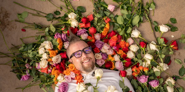 Man lying on floor with different colored roses around his head and face.
