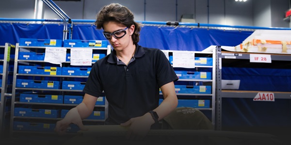 Young man with brown hair in navy polo works at a workbench