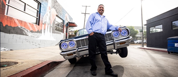 Man leans against the front of a tipped low rider.