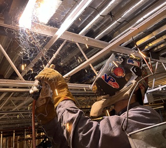 Man with helmet on welding metal with sparks flying.