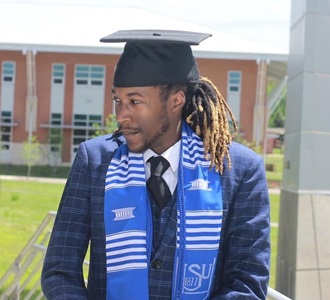 Male student on athletic field with graduation cap and scarf