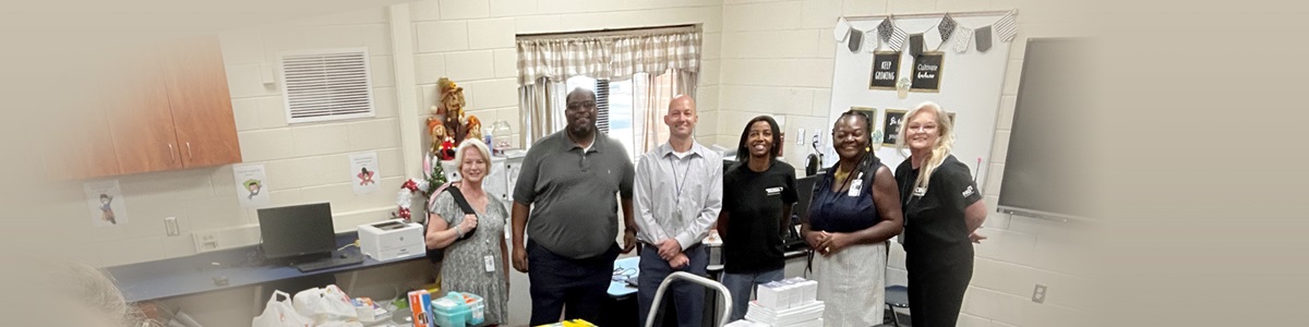 several people lined up in a classroom filled with donations