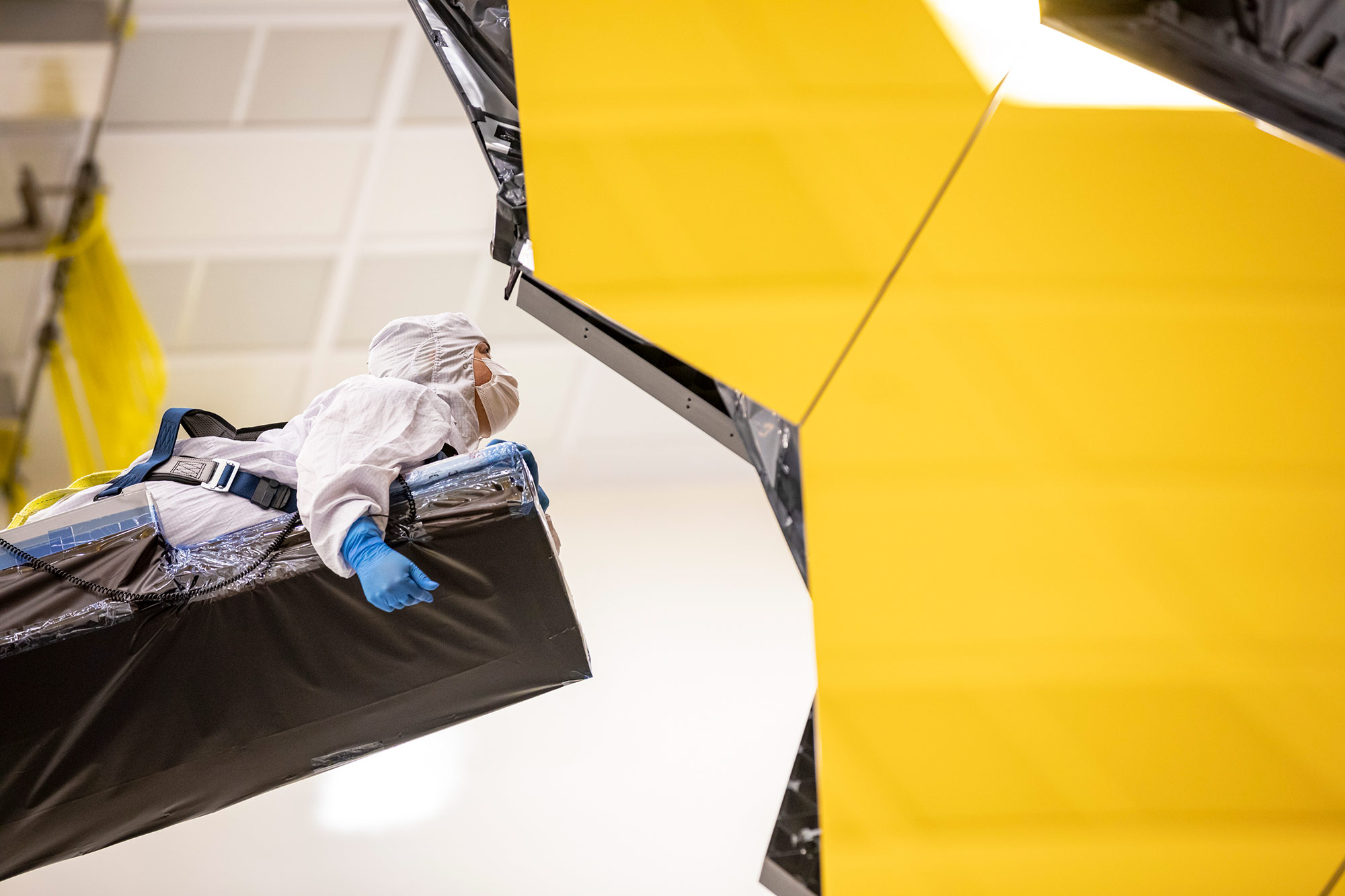 Creating-Zero-G-Crane A person in a clean suit lays on a crane to access the James Webb Space Telescope