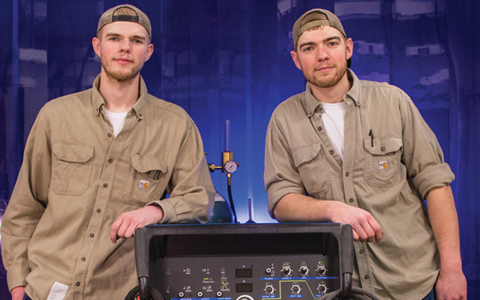 Two Caucasian Males leaning on manufacturing equipment