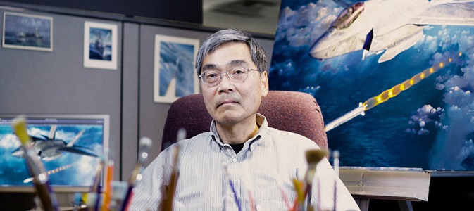 man wearing glasses surrounding by paint brushes