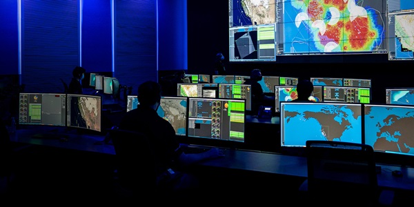Advanced Networking Technology – hero Large command center with multiple computer screens and people monitoring data.