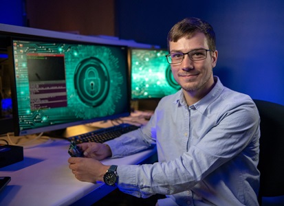 Artificial Intelligence Helps Protect Troops in Denied GPS Environments a man wearing glasses sits at dual monitors and looks directly at the camera