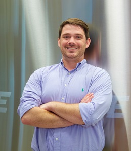 white male with arms crossed over his chest, leaning against a shiny wall