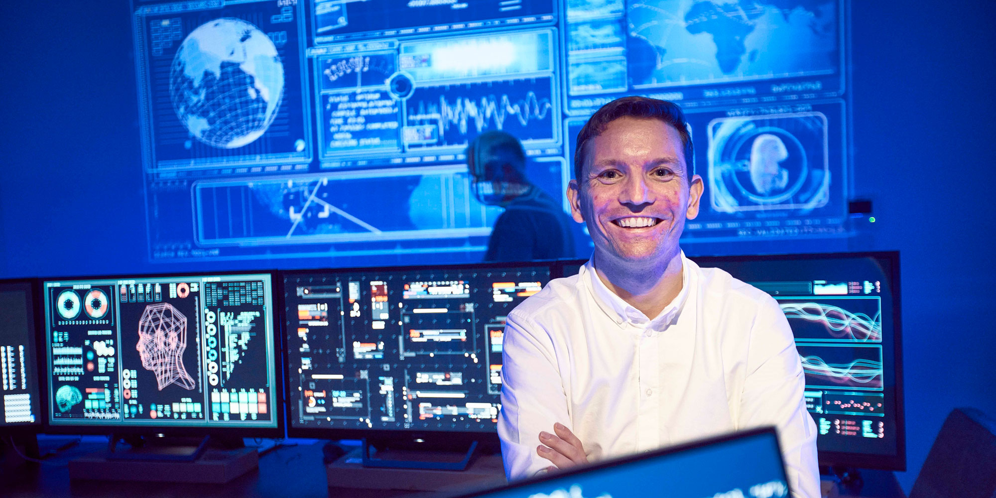 Employee in dark room illuminated by digital screens.
