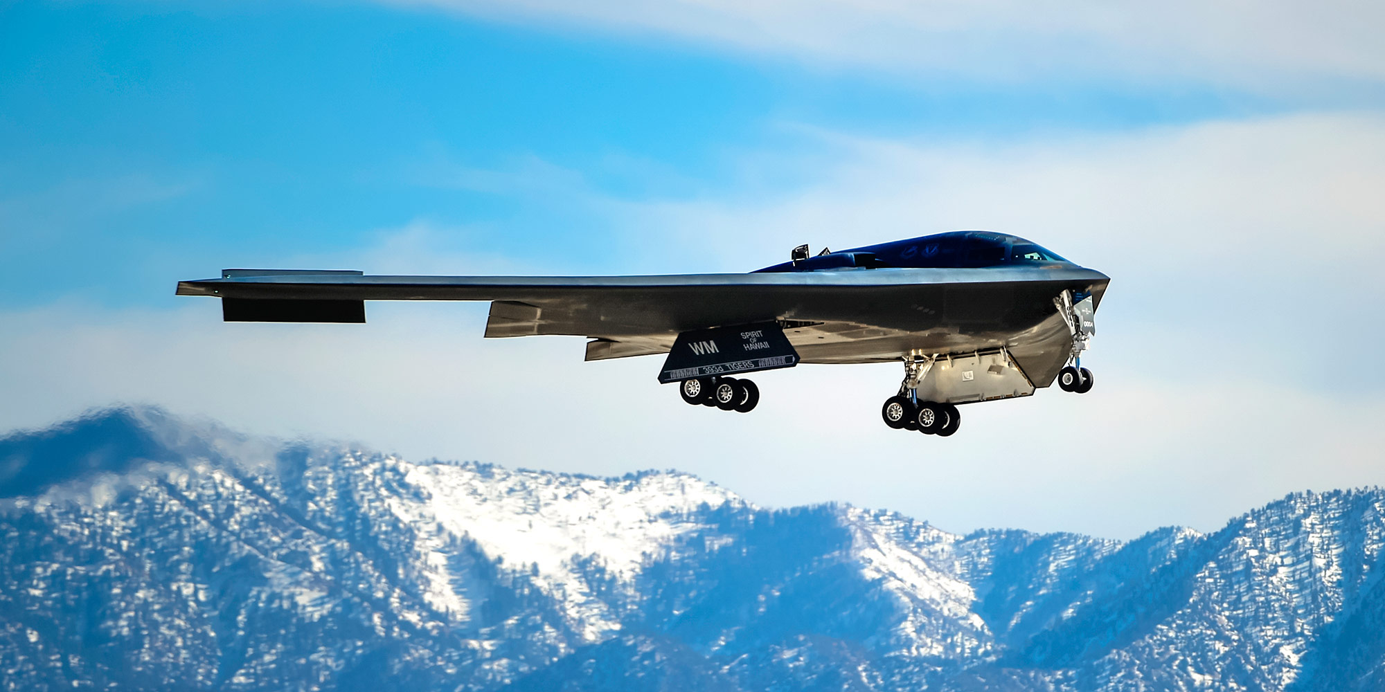 B-2 Spirit Stealth Bomber Image gallery hero image B-2 Spirit Stealth Bomber flying with snow capped mountains in background