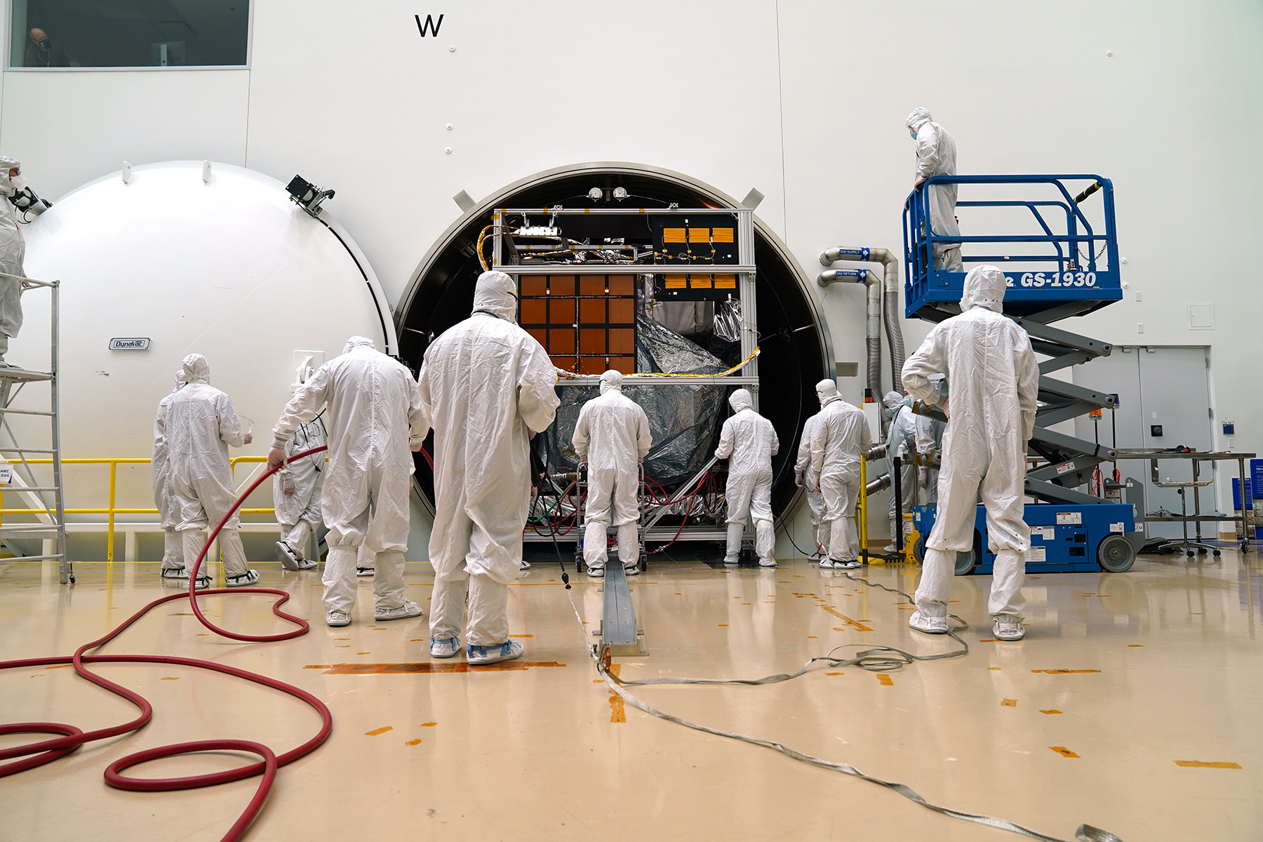 L9-TVAC_2021-3 Engineers facing forward in full covering lab coats are preparing a satellite for testing
